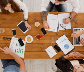Mesa vista desde arriba de varias personas reunidas con móviles, tablet y ordenador