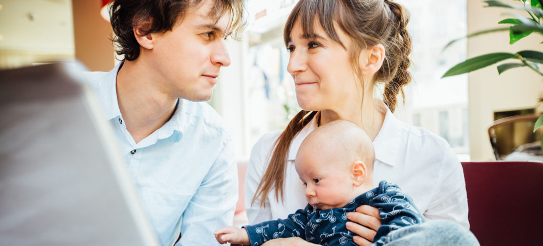 Pareja mirándose fijamente a los ojos mientras la mujer sostiene a un bebé en brazos